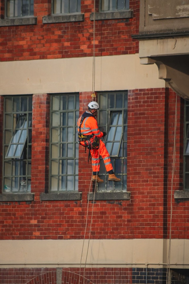 A rope access technician working at height on a building facade, wearing a harness and helmet